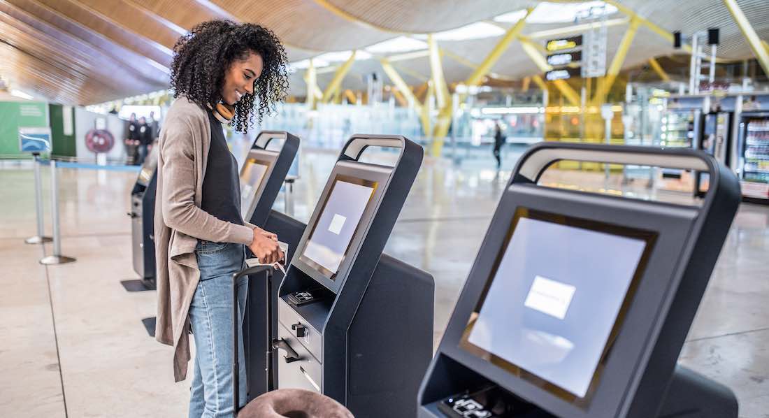 Junge Frau beim Geldabheben im Ausland, im Hintergrund ein Flughafen-Terminal