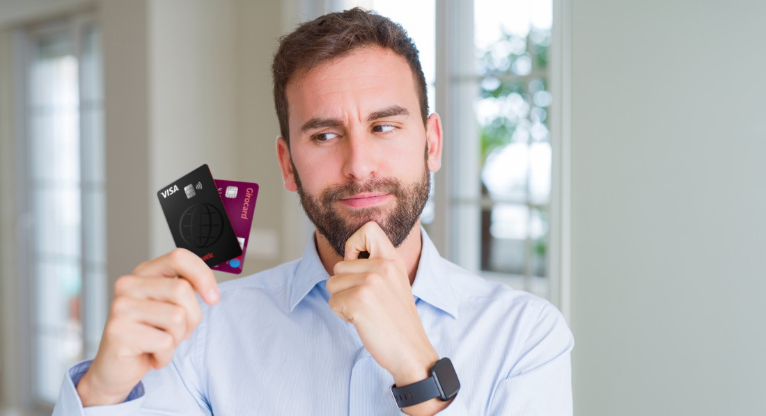 Mann sieht auf Kreditkarte und Girocard in seiner Hand