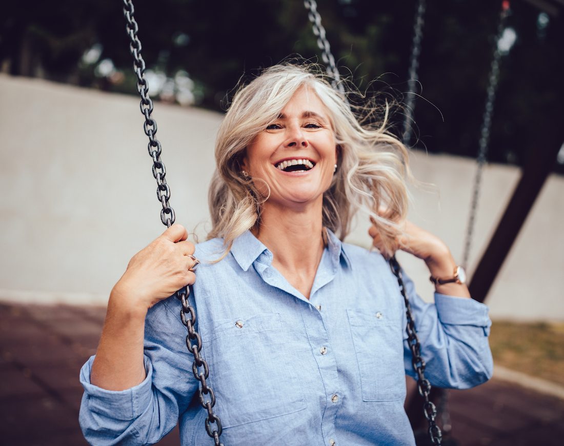 Rentenlücke schließen: Frau mit grauen Haaren sitzt lachend auf einer Schaukel
