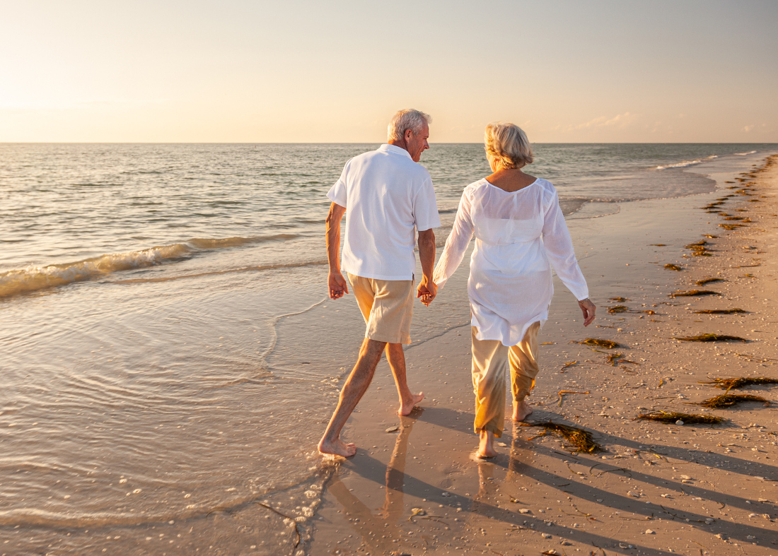 Ein Paar in Rente geht händchenhaltend beim Sonnenuntergang am Strand spazieren