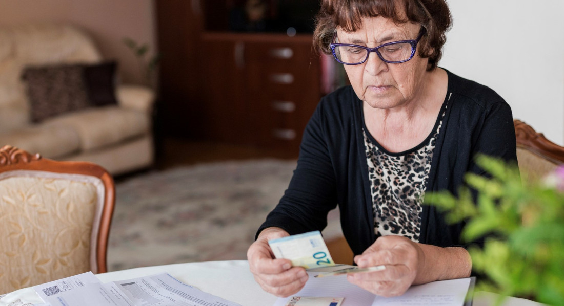 Alte Frau sitzt am Esstisch mit Rechnungen und zählt ihr Geld