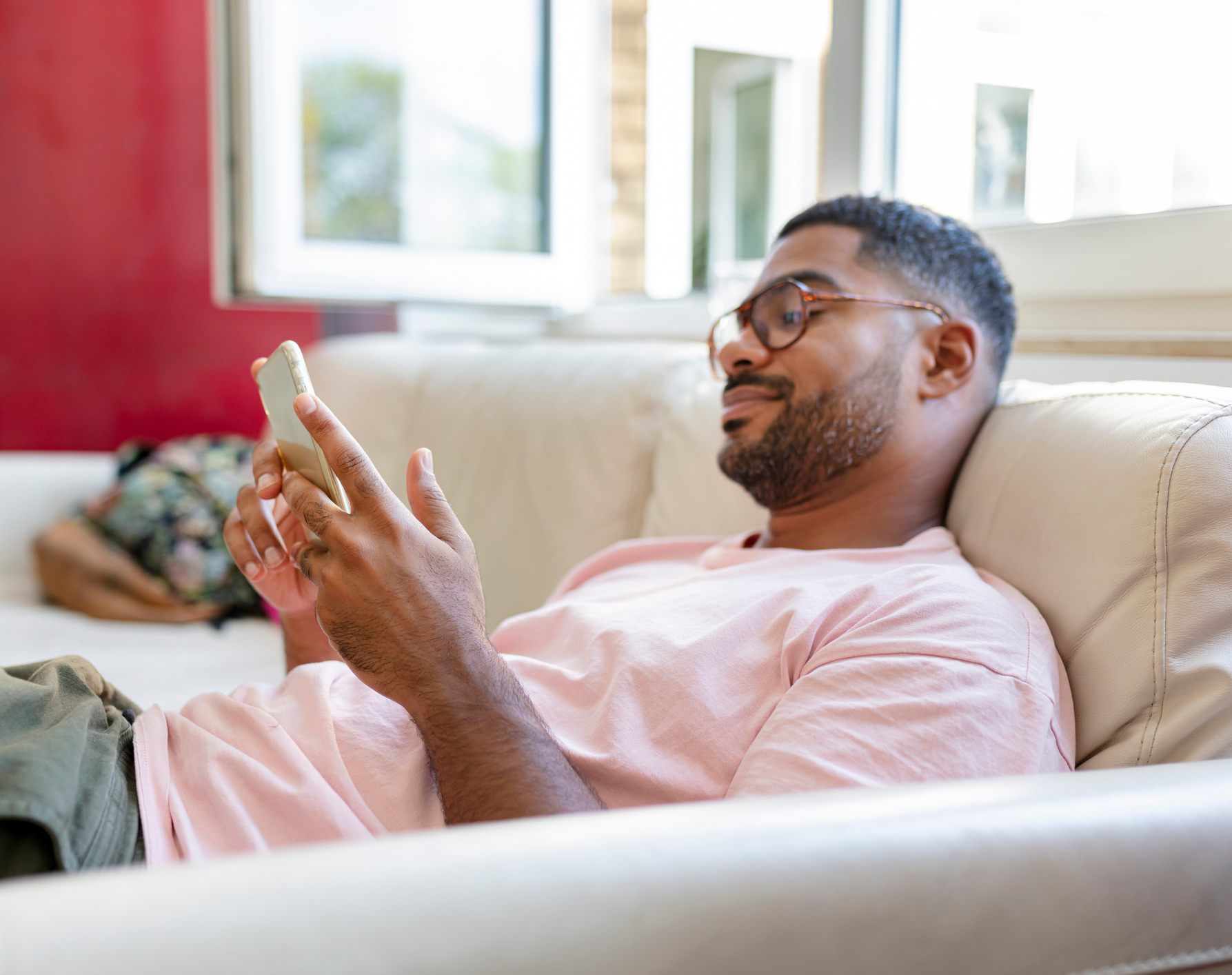 Mann lehnt auf einem Sofa und schaut in ein Smartphone