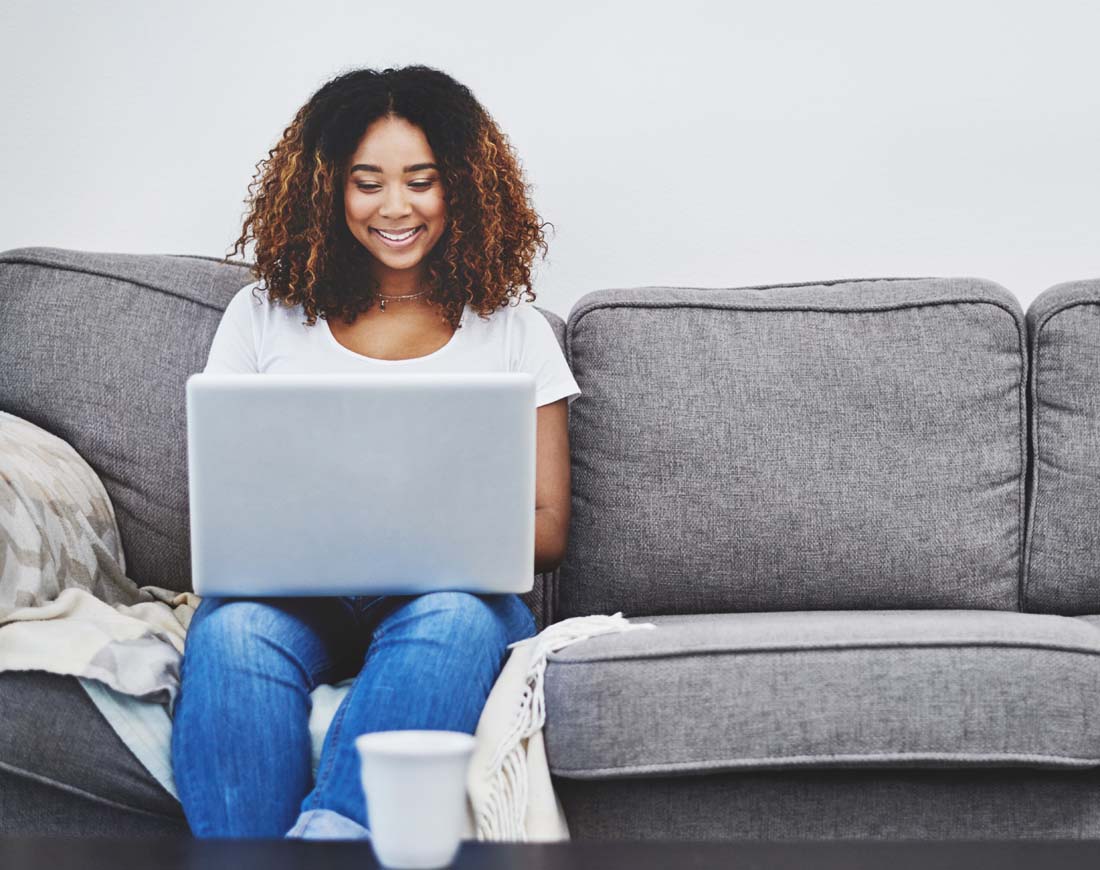Junge Frau sitzt auf dem Sofa und surft mit ihrem Laptop im Internet
