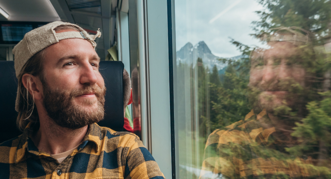 Ein Mann sitzt im Zug, der durch einen Wald fährt, und genießt die Landschaft durch das Fenster