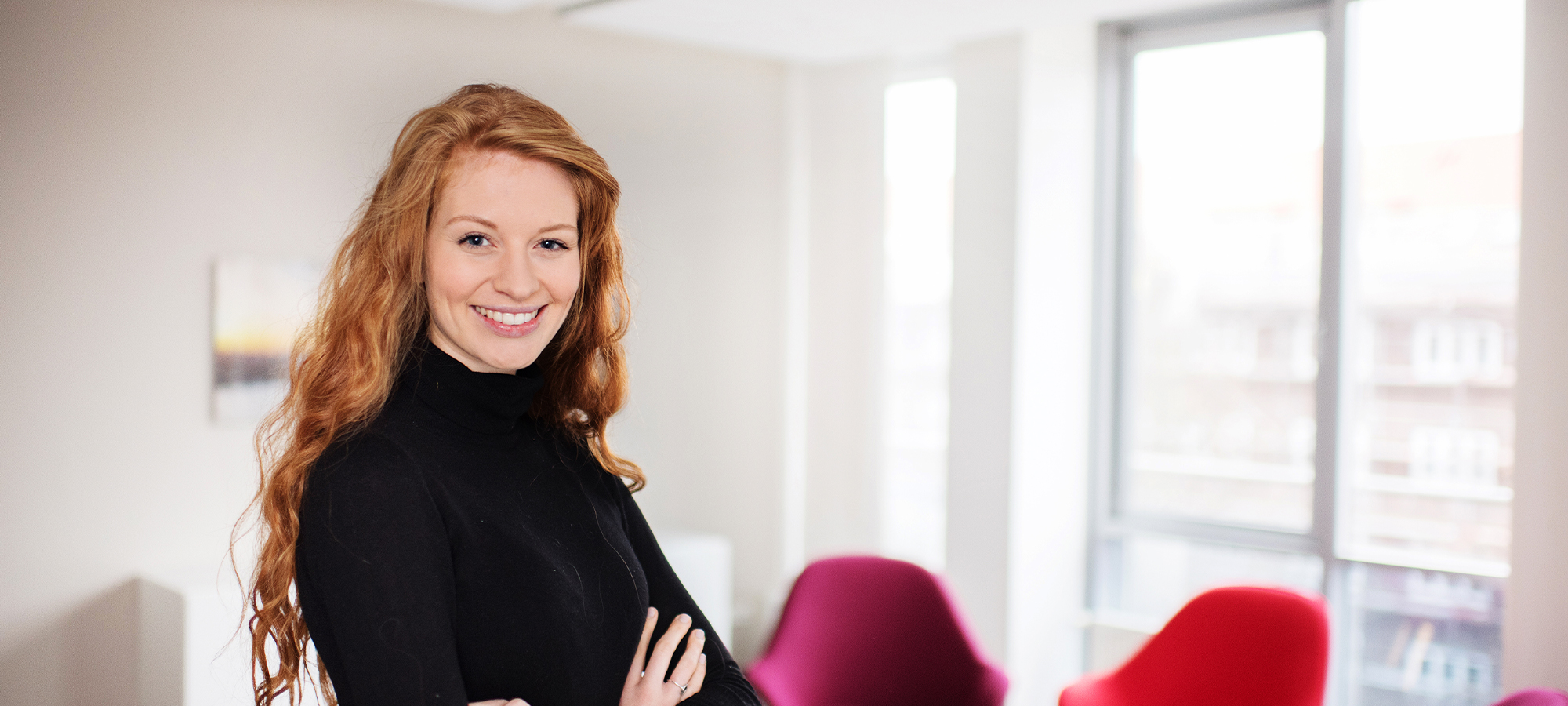 Eine junge Frau steht in einem Büro lächelt in die Kamera.