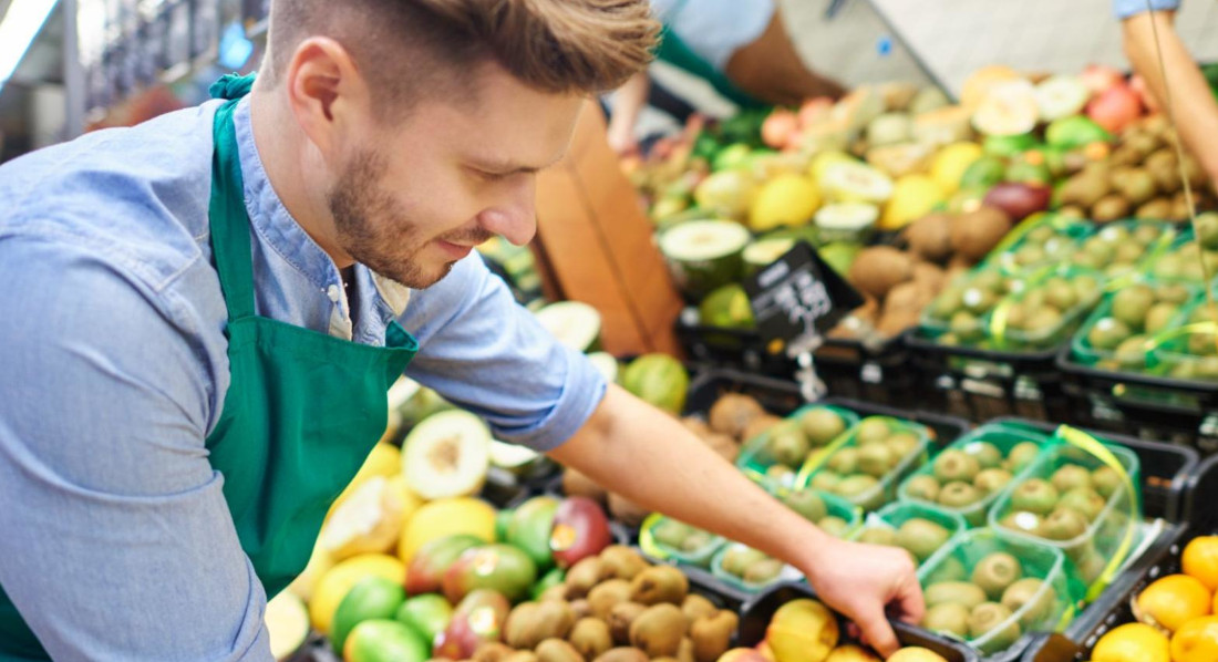 Ein Minijobber füllt im Supermarkt das Obstregal nach