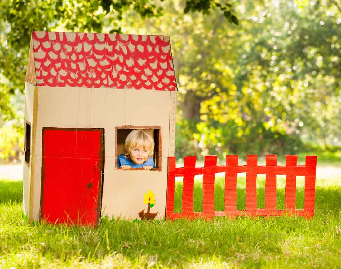 Kleiner blonder Junge schaut aus dem Fenster eines Spielhauses aus Pappe