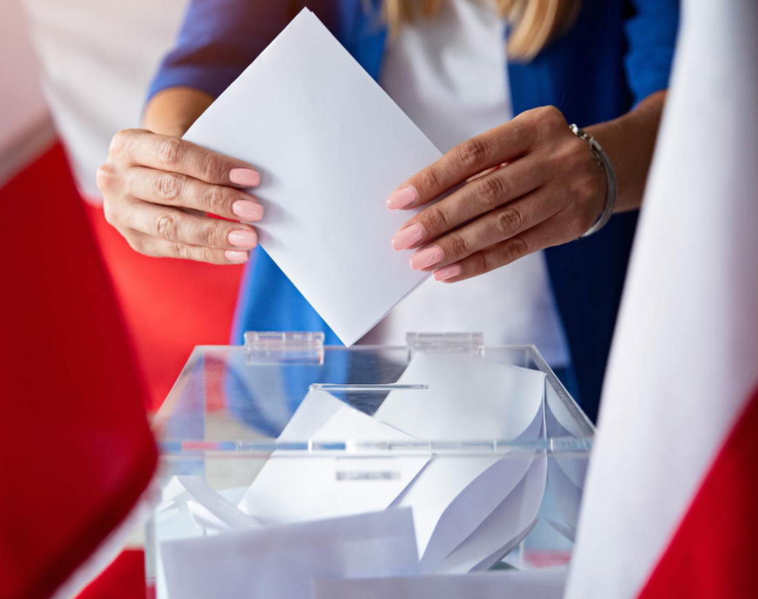 Frau legt gefalteten Wahlzettel in eine Wahlurne
