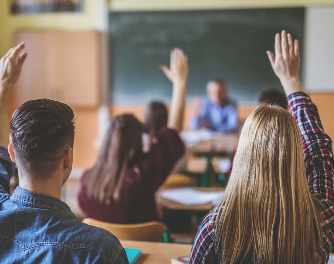 Erwachsene Schüler in einem Klassenraum heben den Arm, um eine Frage zu beantworten