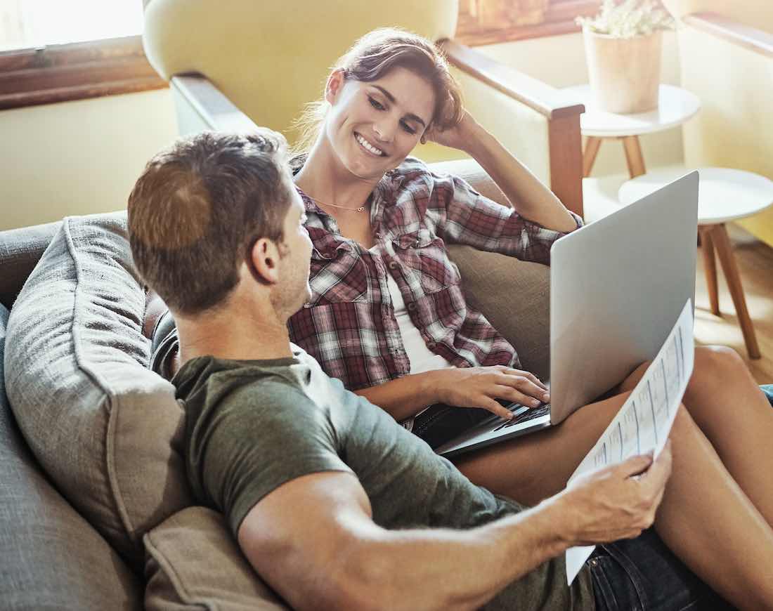 Diese Versicherungen braucht man wirklich: Ein Paar sitzt auf dem Sofa mit einem Laptop und Dokumenten