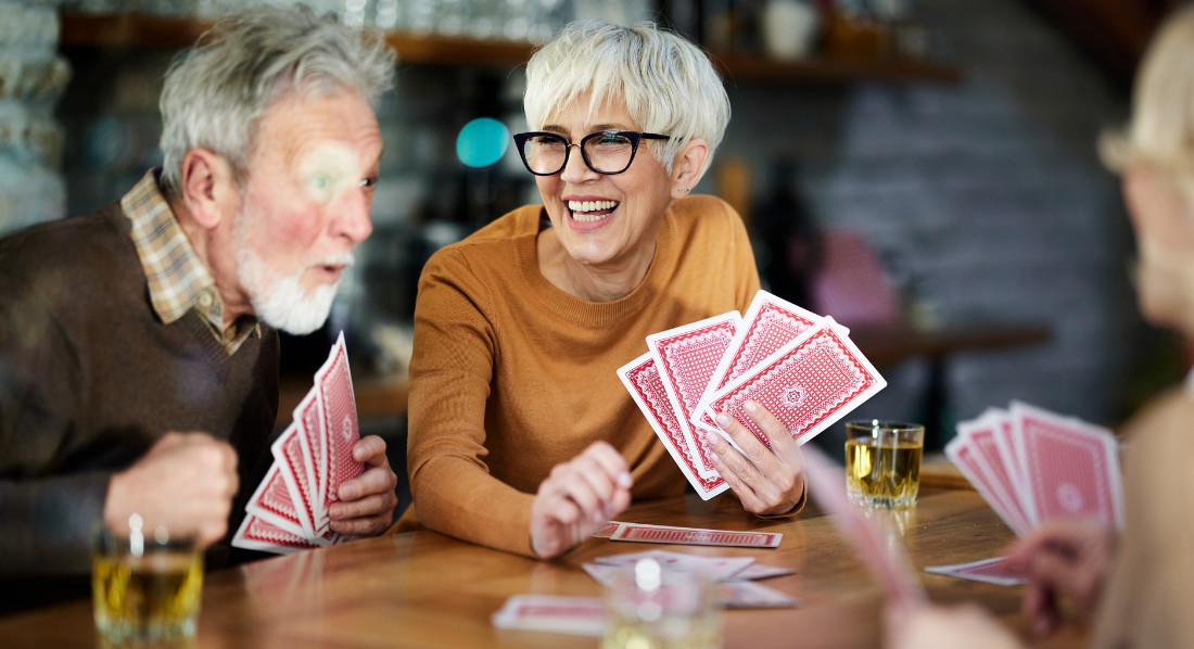 Drei ältere und ausgelassene Menschen spielen Karten an einem Tisch im Restaurant