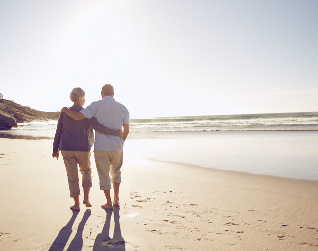 Ein älteres Paar schlendert Arm in Arm den Strand entlang
