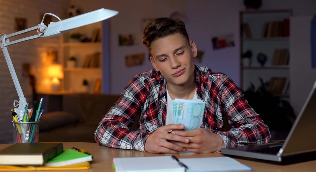 Ein Jugendlicher sitzt an seinem Schreibtisch und zählt zufrieden Geldscheine