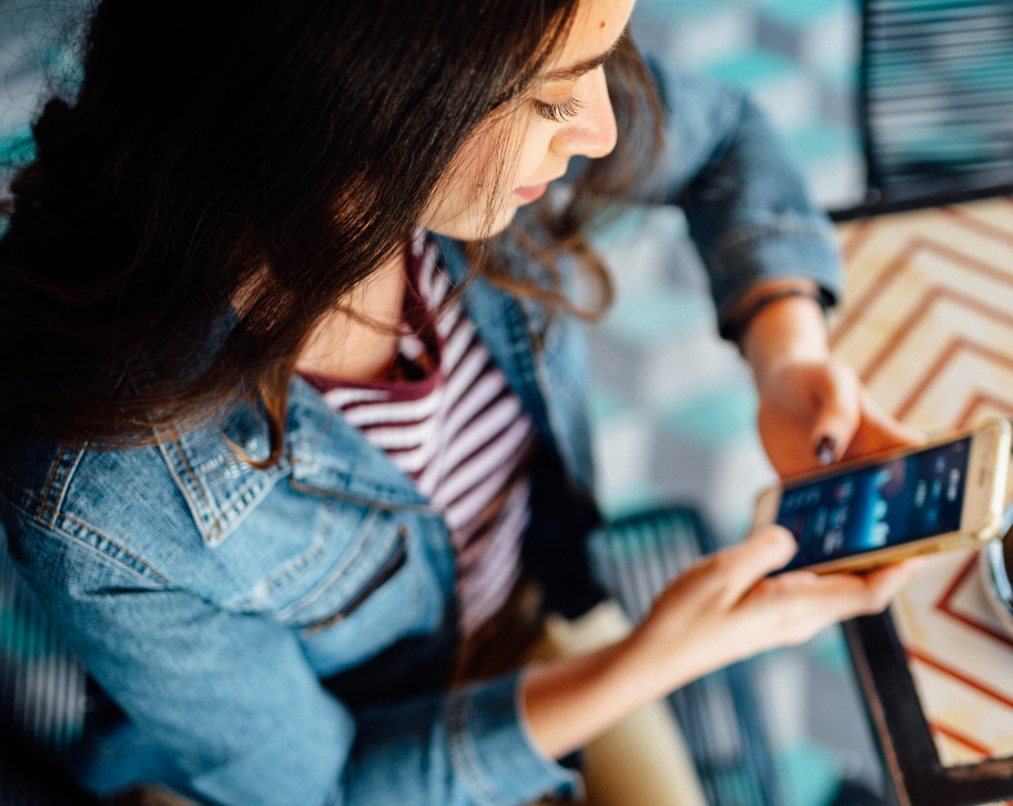 Eine junge Frau sitzt mit einem Cappuccino im Café und hält ihr Smartphone mit einer Finanz-App auf dem Display