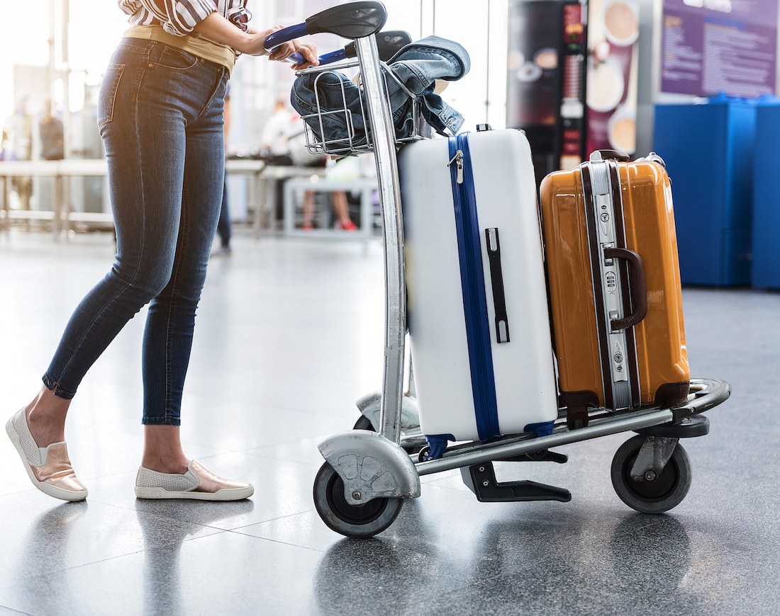 Frau schiebt Kofferkuli voll mit Gepäck durch den Flughafen