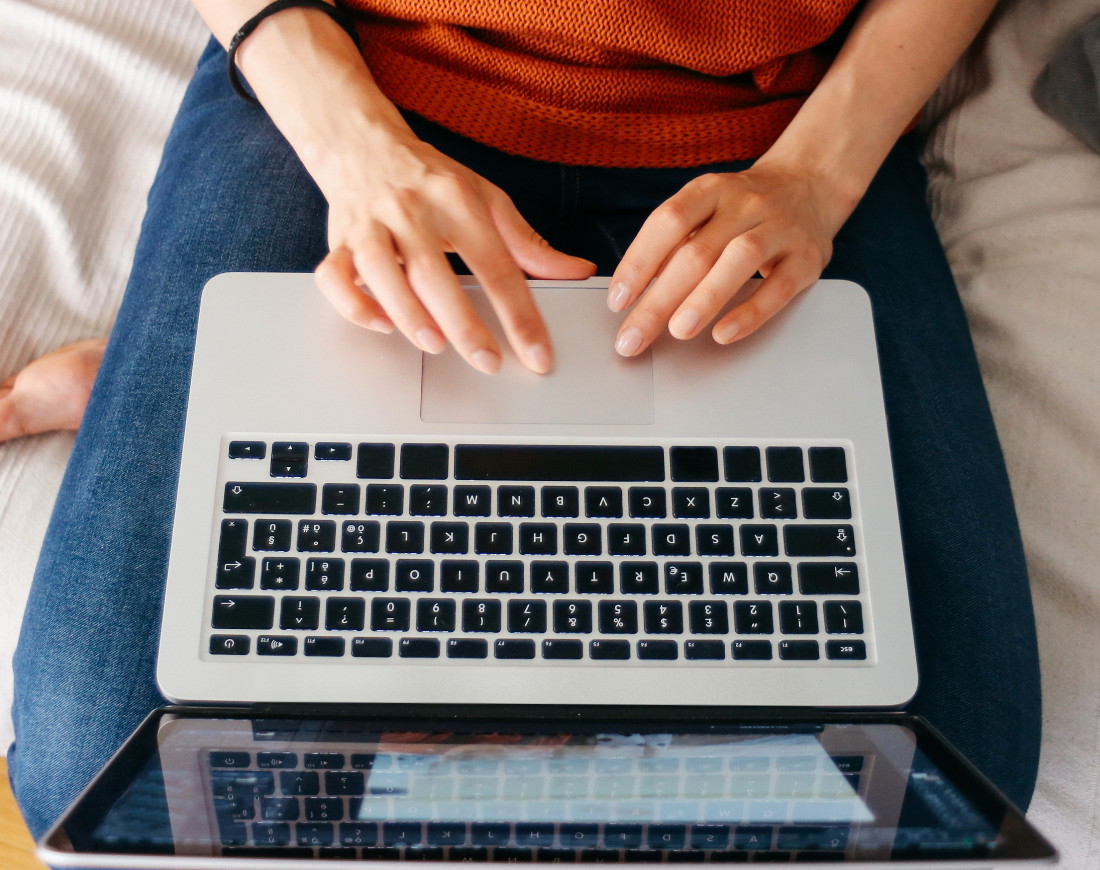 Frau sitzt auf dem Sofa mit Laptop auf dem Schoß.