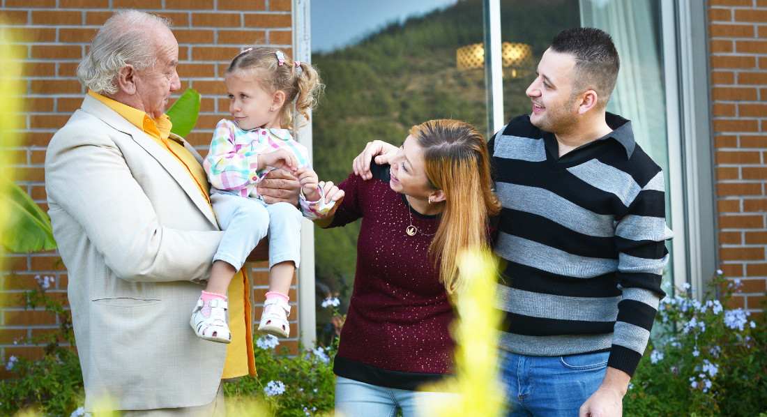 Familie steht im Garten vor dem Haus, Opa trägt Enkelin auf dem Arm
