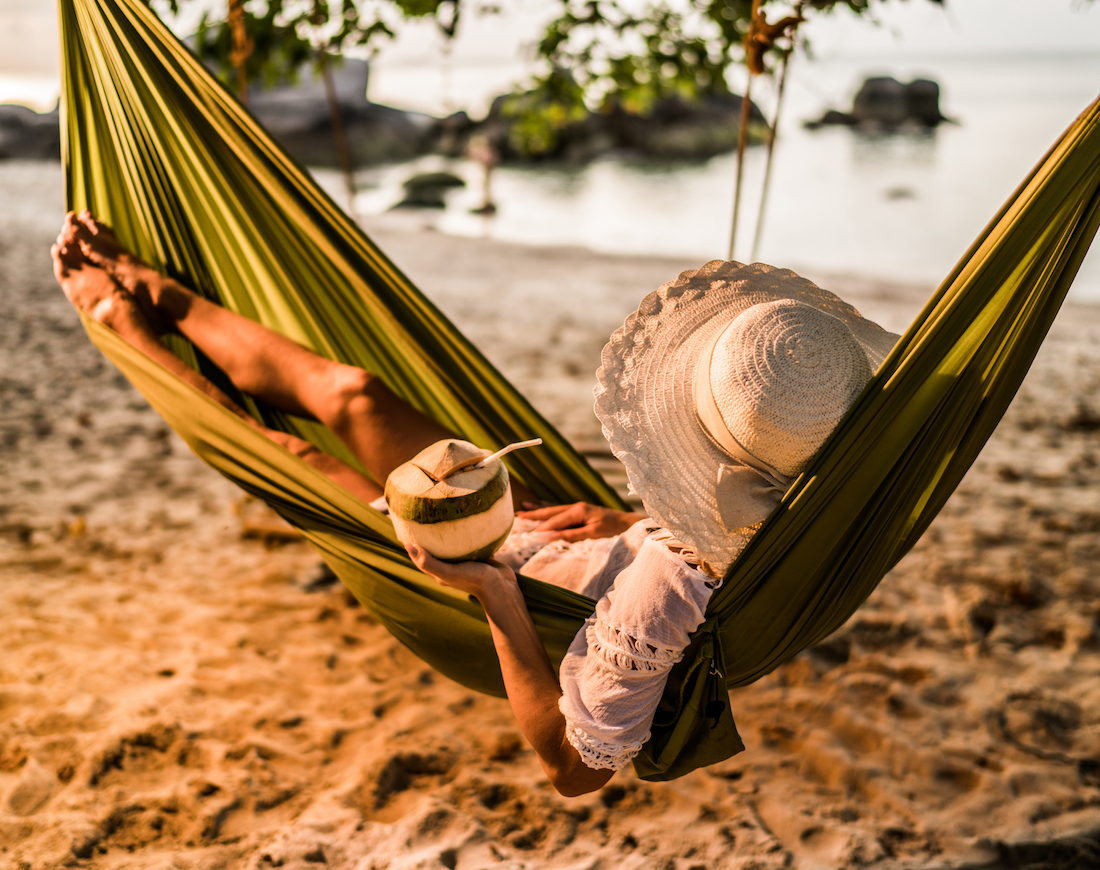 Frau entspannt mit einem Drink in einer Kokosnuss in einer Hängematte an einem exotischen Strand