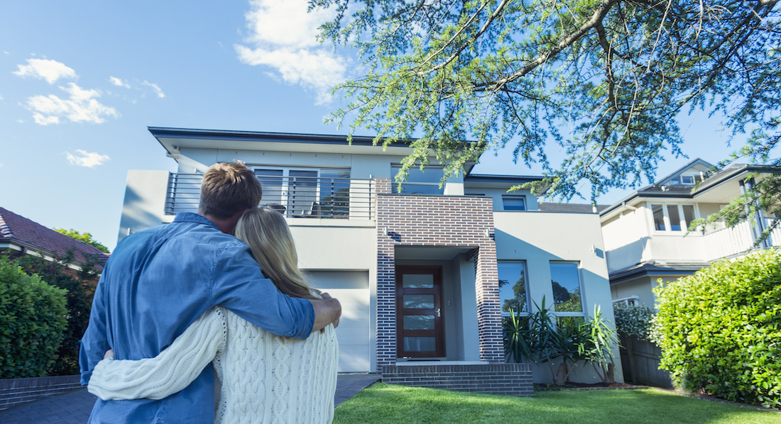 Das Haus ist versichert: Ein Ehepaar steht Arm in Arm und blickt auf sein Haus