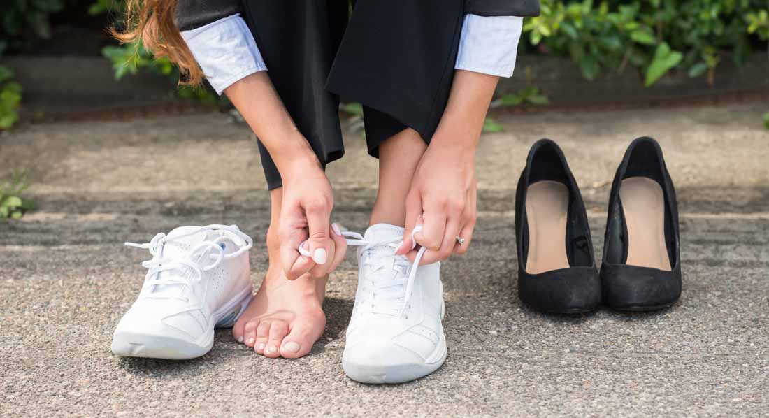 Frau zieht ihre Pumps aus und zieht stattdessen Turnschuhe an
