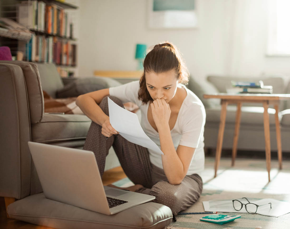 Eine Frau sitzt nachdenklich mit einer Rechnung am Laptop