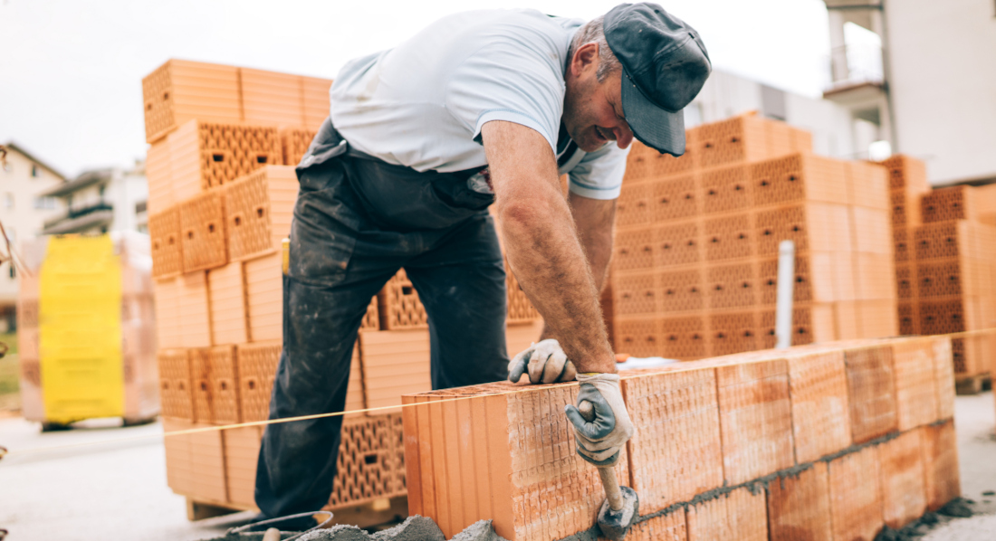 Handwerker mit Kappe mauert in Schwarzarbeit eine Wand eines neuen Hauses