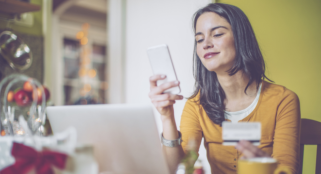 Eine junge Frau sitzt vor ihrem Laptop und nutzt mit ihrem Smartphone das ChipTAN-Verfahren