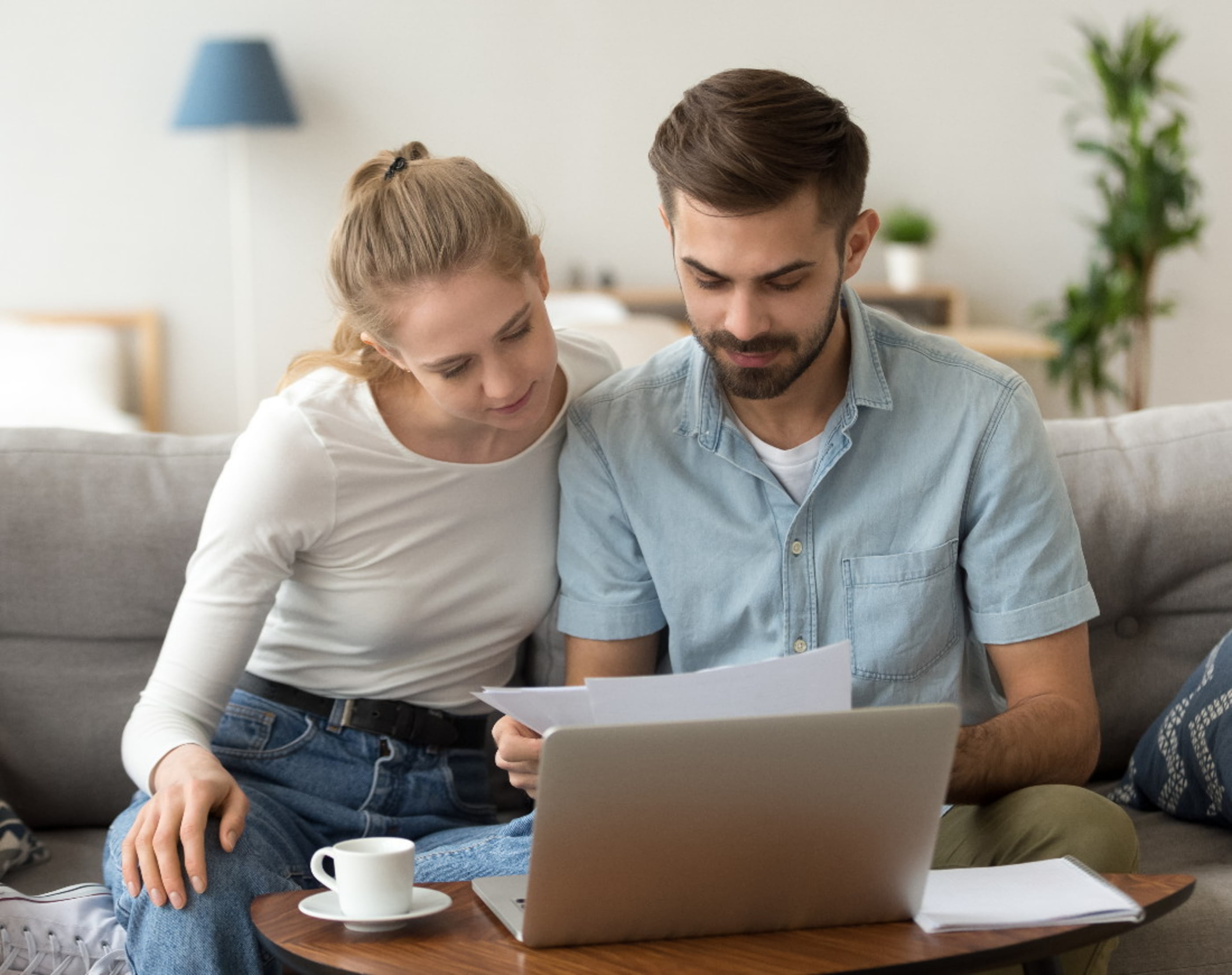 Pärchen sitzt vor dem Laptop und hält die Kreditantragsunterlagen in den Händen
