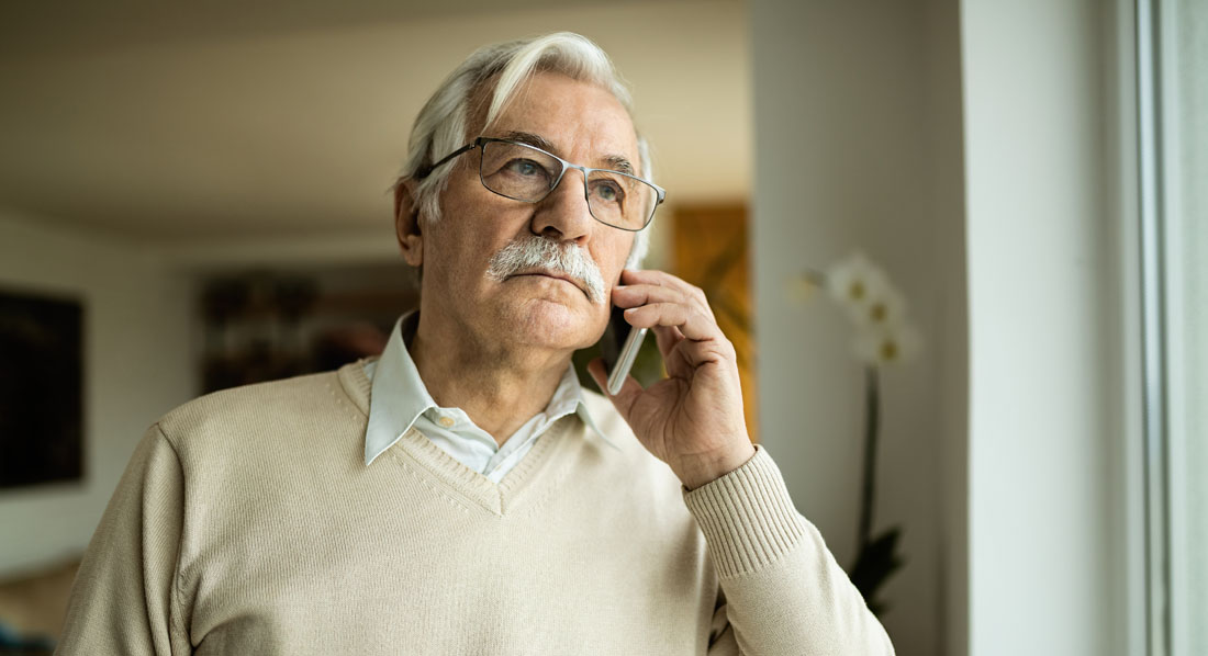 Ein älterer Mann telefoniert zu Hause mit seinem Handy und blickt nachdenklich aus dem Fenster