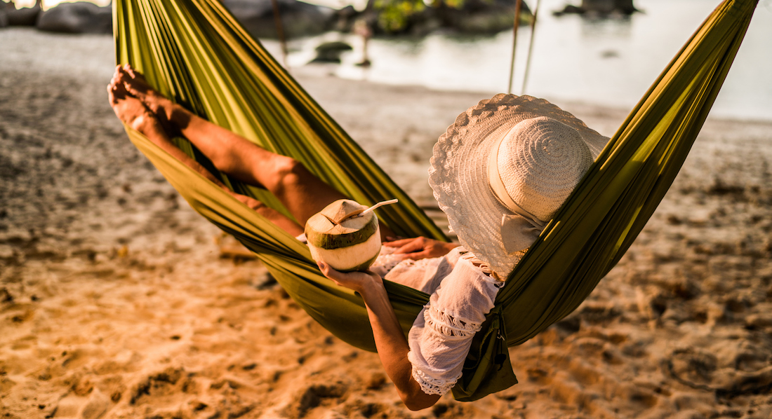 Frau entspannt mit einem Drink in einer Kokosnuss in einer Hängematte an einem exotischen Strand