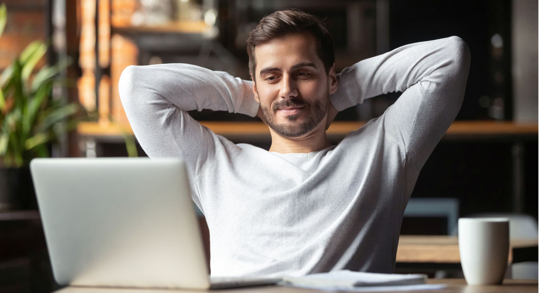 Ein junger Mann sitzt auf einem Sofa und liest in seinem Laptop eine gute Nachricht