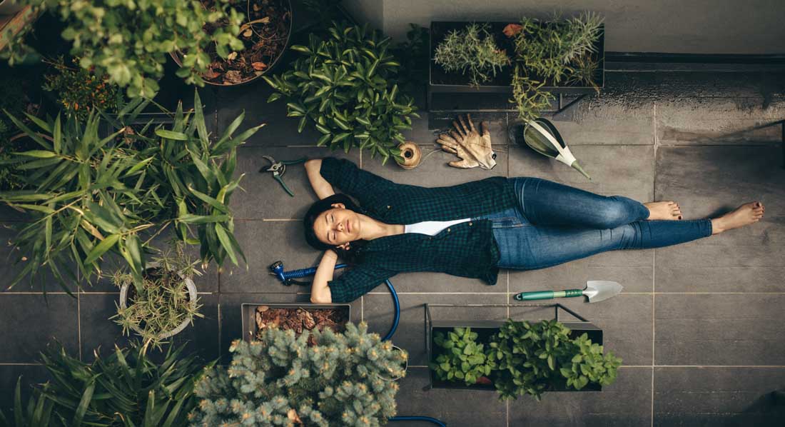 Junge Frau liegt zwischen mehreren Blumenkübeln mit selbst angebauten Pflanzen