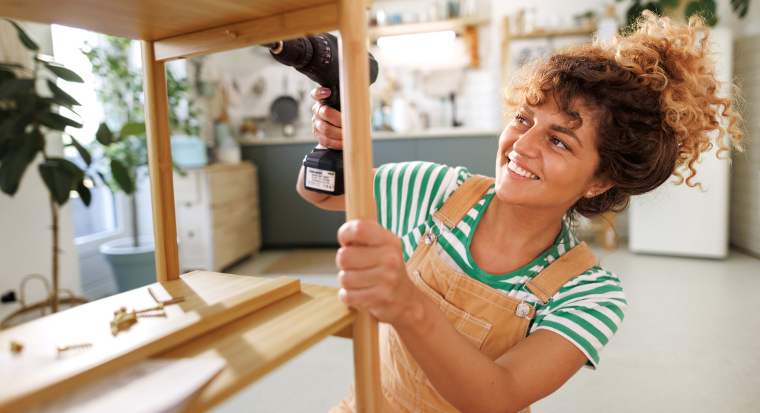 Eine junge Frau schraubt mit einem Akkuschrauber ein Regal in ihrer Wohnung zusammen