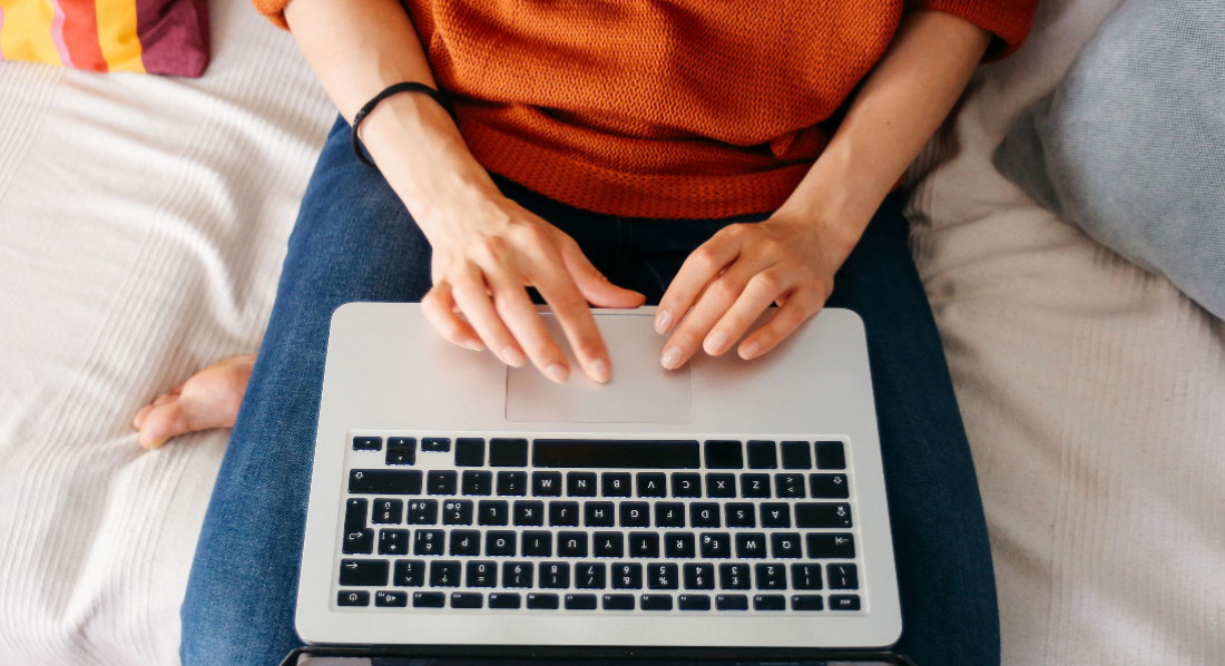 Frau sitzt auf dem Sofa mit Laptop auf dem Schoß.