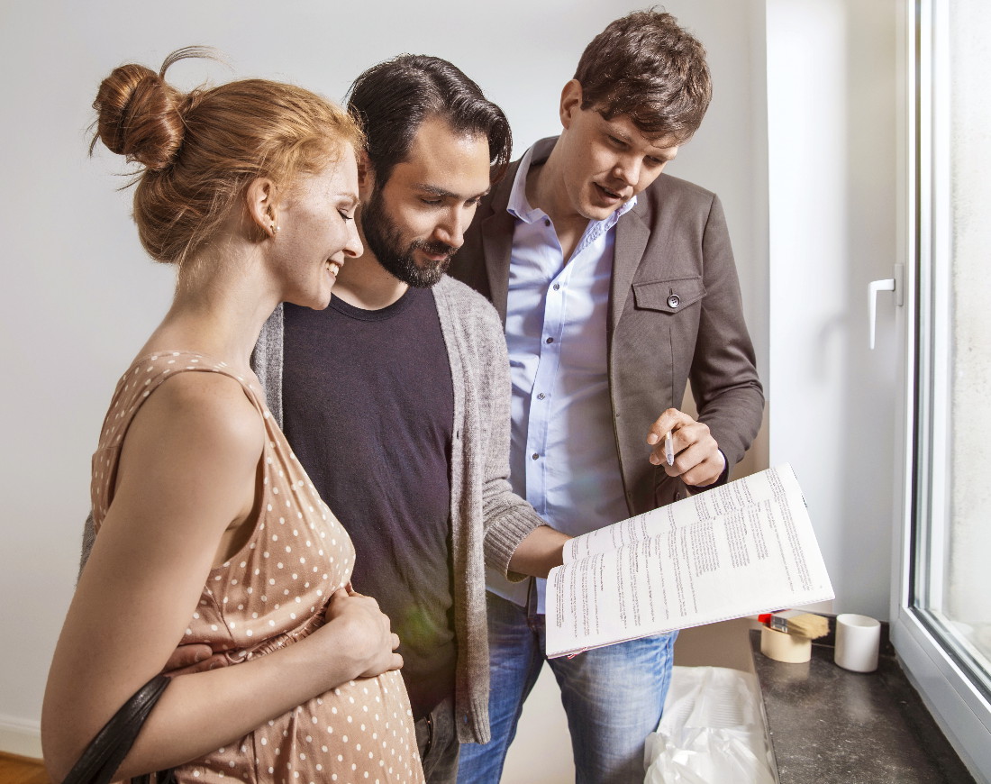 Schwangere junge Frau und Partner mit Berater lesen Finanzplan bei Eigenheimbesichtigung