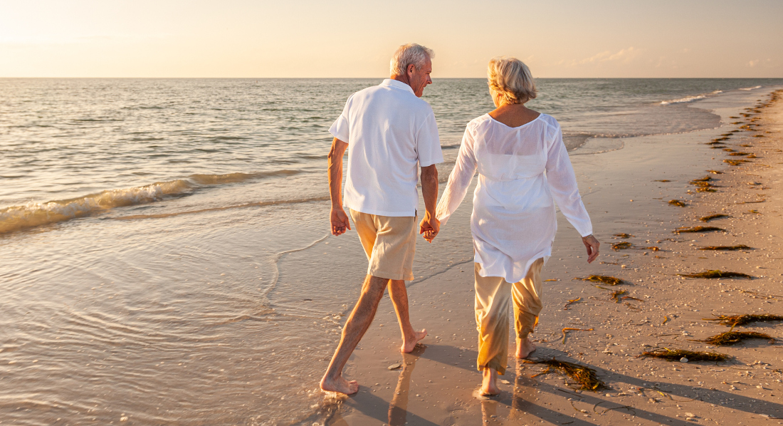 Ein Paar in Rente geht händchenhaltend beim Sonnenuntergang am Strand spazieren