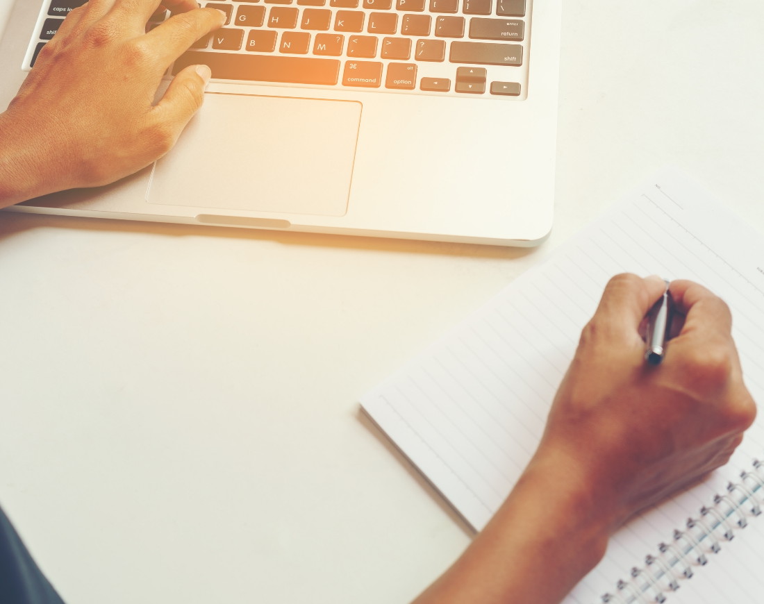 Eine Frau tippt ihren Antrag auf eine Renteninformation mit der linken Hand in einen Laptop und macht sich Notizen mit der rechten Hand.