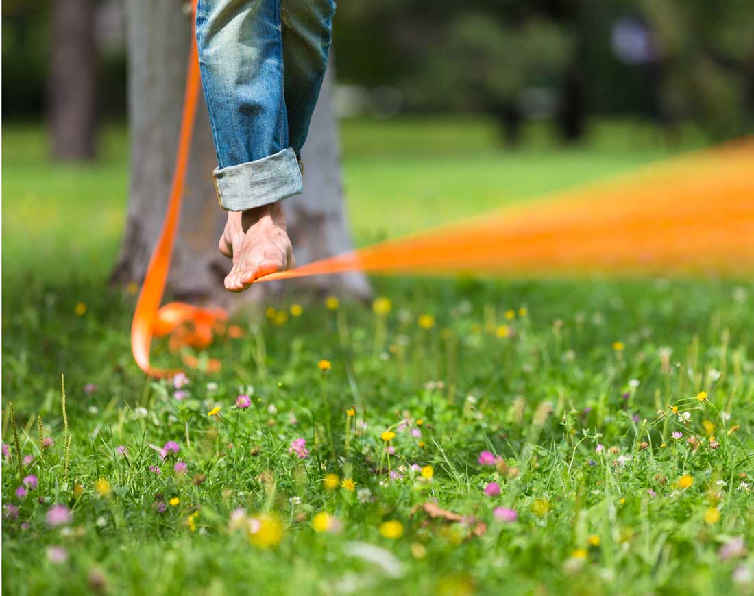 Eine Mann balanciert auf einer über einer Blumenwiese gespannten bodennahen Slackline