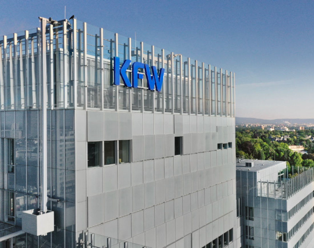 Ansicht des KfW-Hauptgebäudes in Frankfurt am Main. Man sieht ein großes Glasgebäude im Sonnenuntergang. An der Fassade ein blaues KfW-Logo.