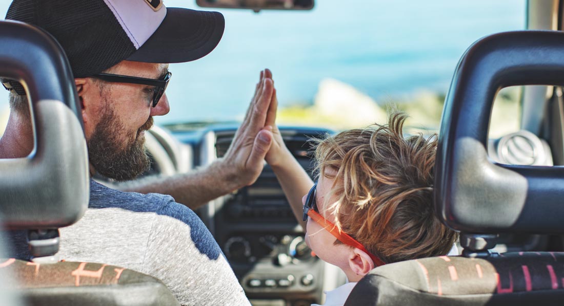 Junger Vater mit kleinem Sohn klatschen sich im Auto sitzend ab