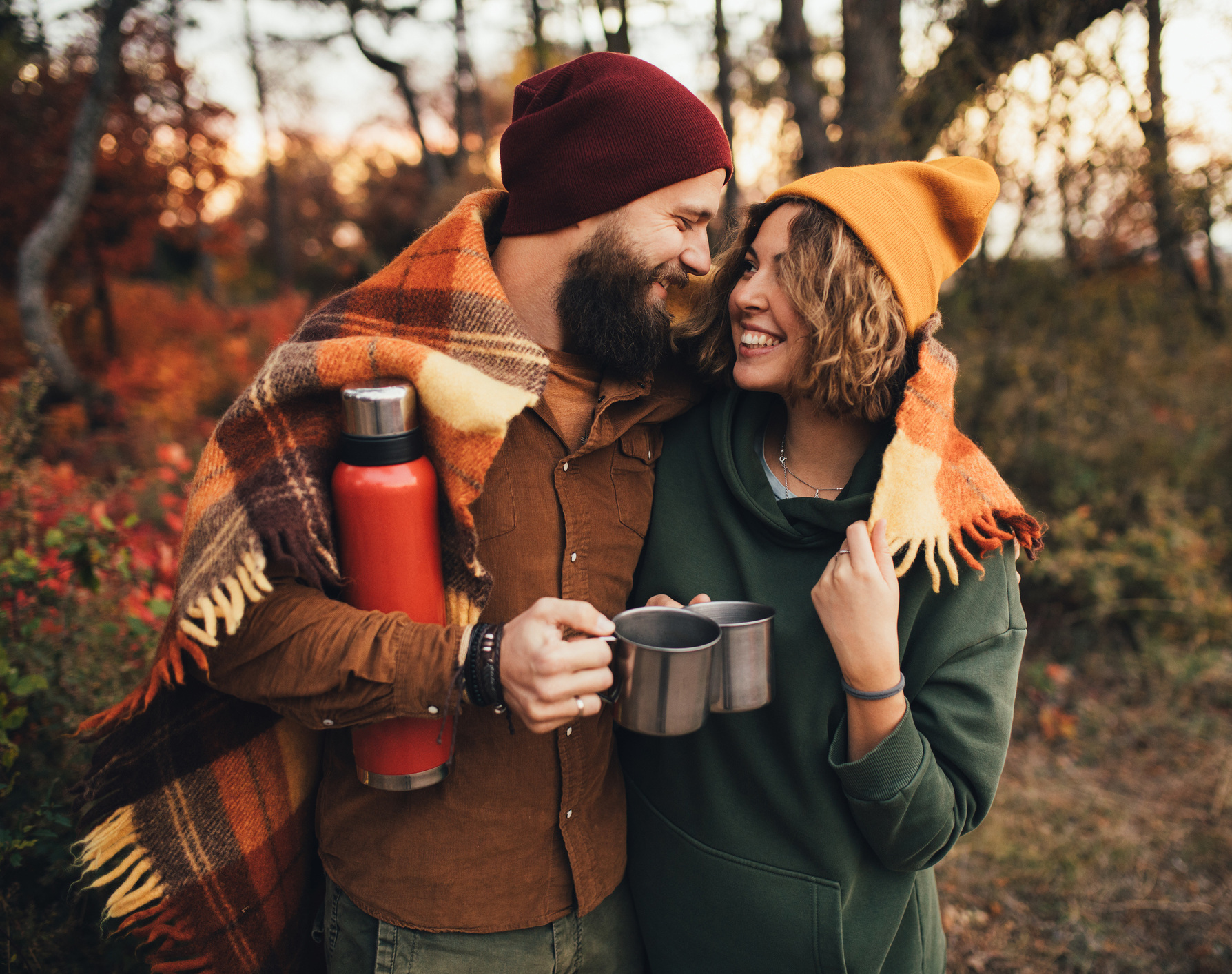 Ein Mann und eine Frau sind in der Natur, umarmen sich und haben Tassen in der Hand