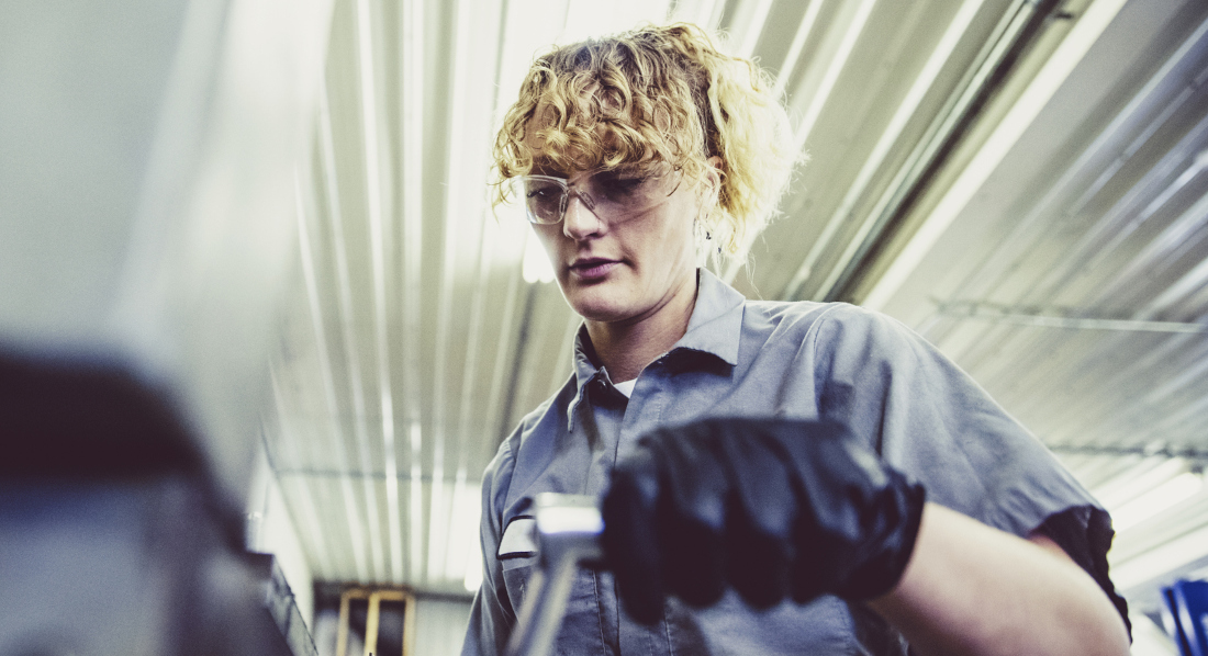 Eine Frau arbeitet mit Schutzbrille an einer schweren Maschine