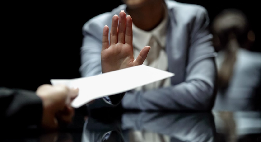 Eine Frau weist mit erhobener Hand ein angebotenes Dokument zurück