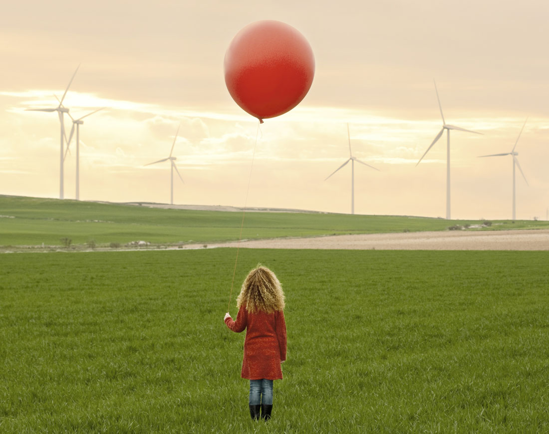 Ein Mädchen auf einer Wiese mit einem Luftballon in der Hand im Hintergrund Windräder
