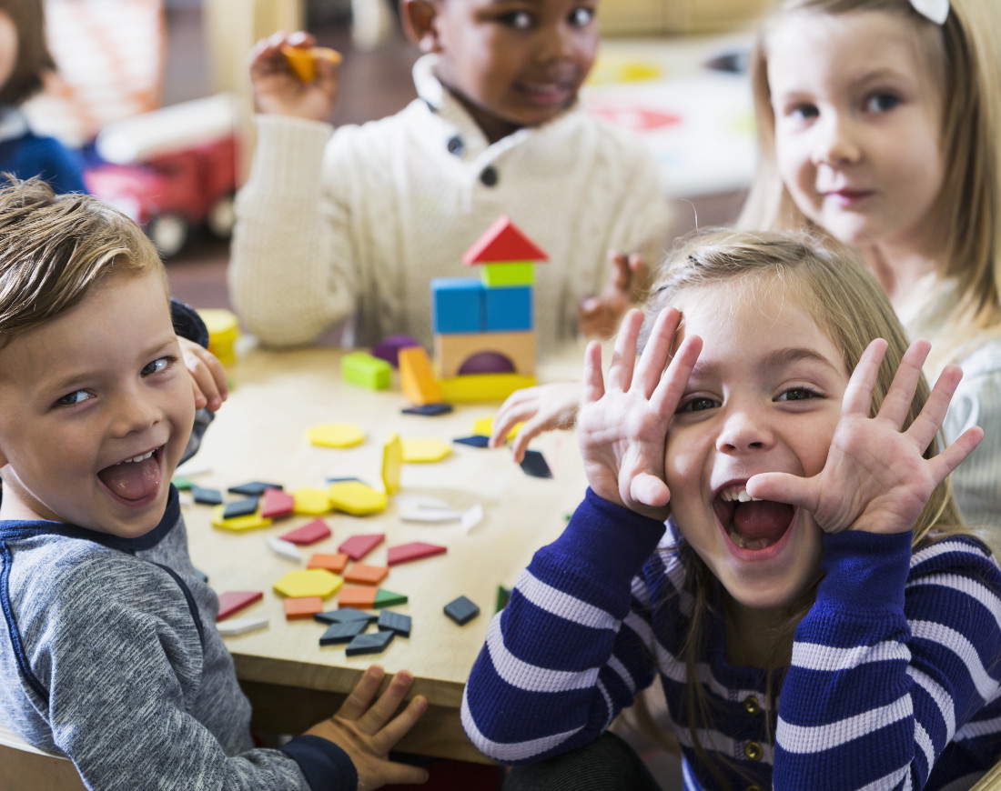 Kindergartenkinder sitzen um einen Tisch und machen Faxen