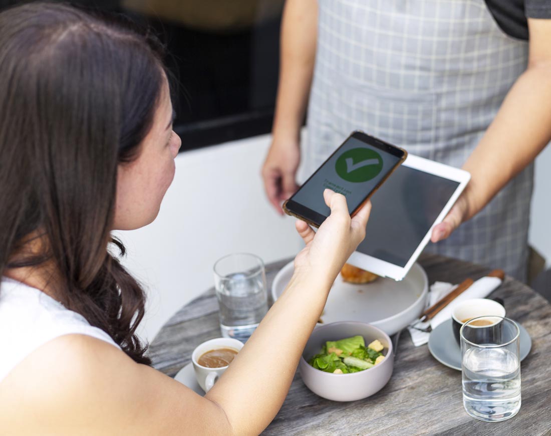 Eine Frau bezahlt in einem Restaurant über die Wallet-App auf ihrem Smartphone