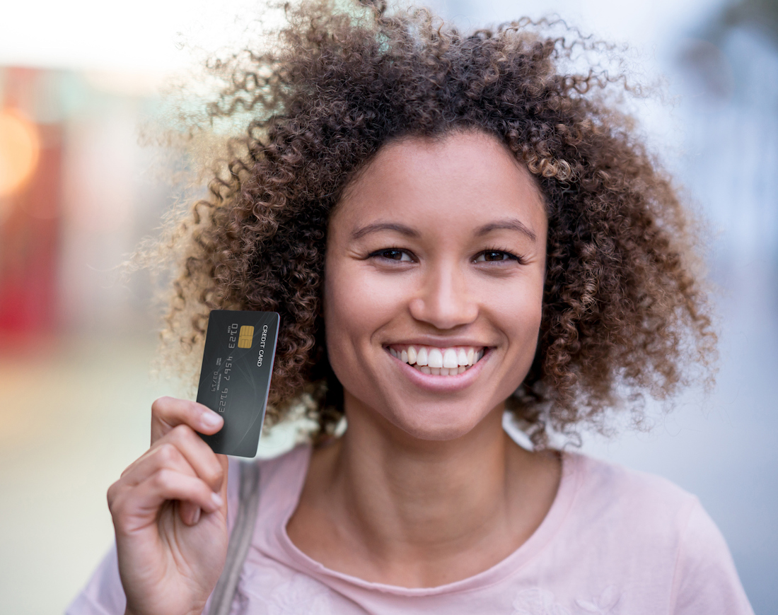 Junge Frau hält lächelnd Kreditkarte in der Hand
