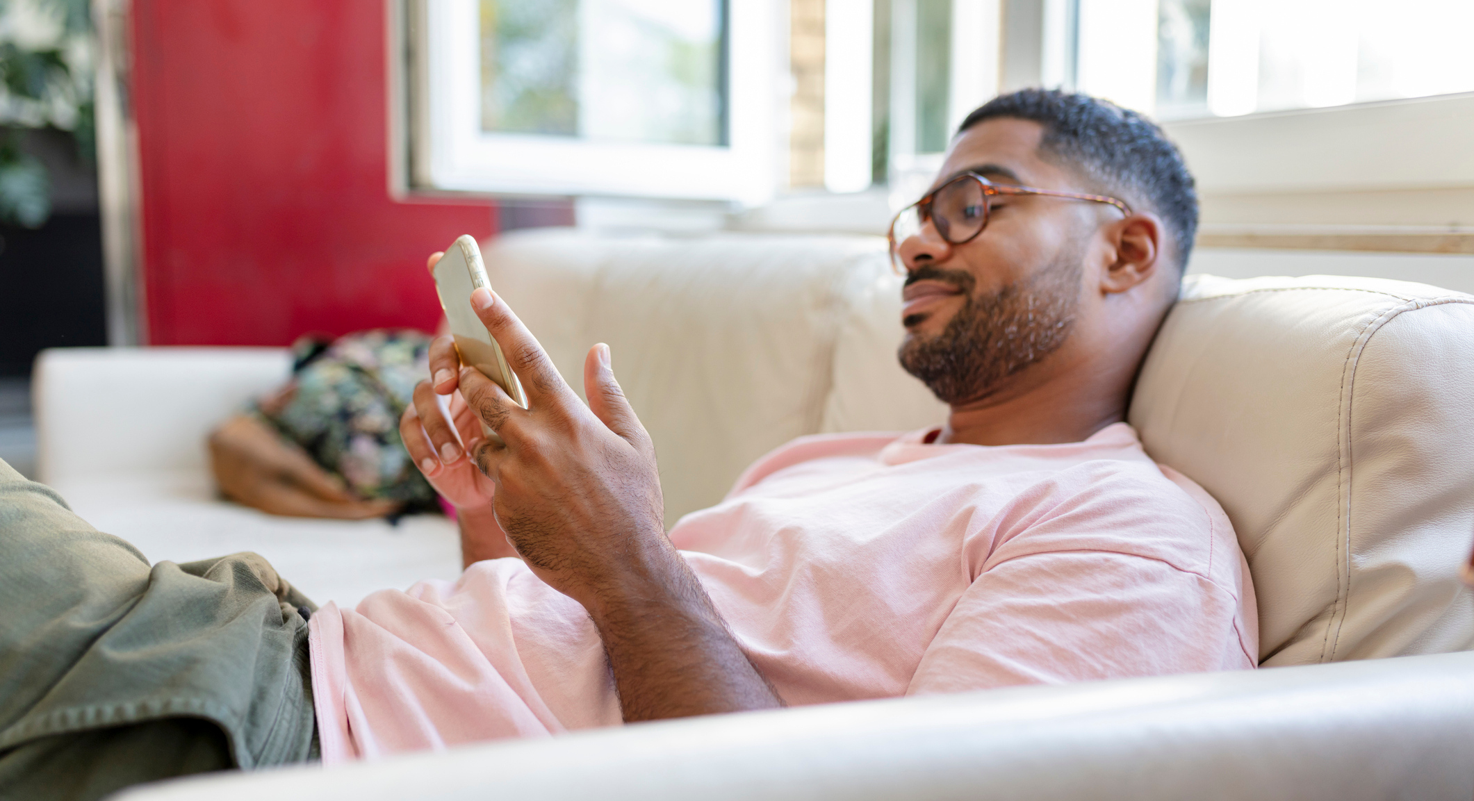 Mann lehnt auf einem Sofa und schaut in ein Smartphone