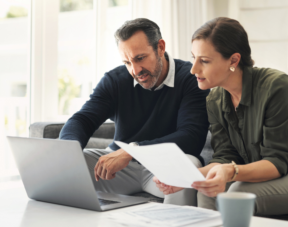 Ein Paar sitzt auf dem Sofa vor einem Laptop mit einem Stapel Finanzdokumente