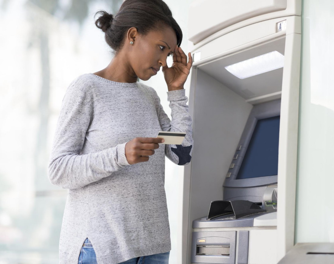 Frau steht ratlos mit ihrer Kreditkarte vor einem Bankautomaten